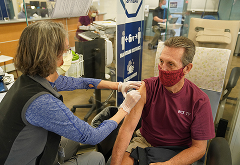 A female nurse administers a vaccine to a male Veteran