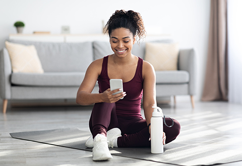 A woman checks her mobile phone while exercising in her living room